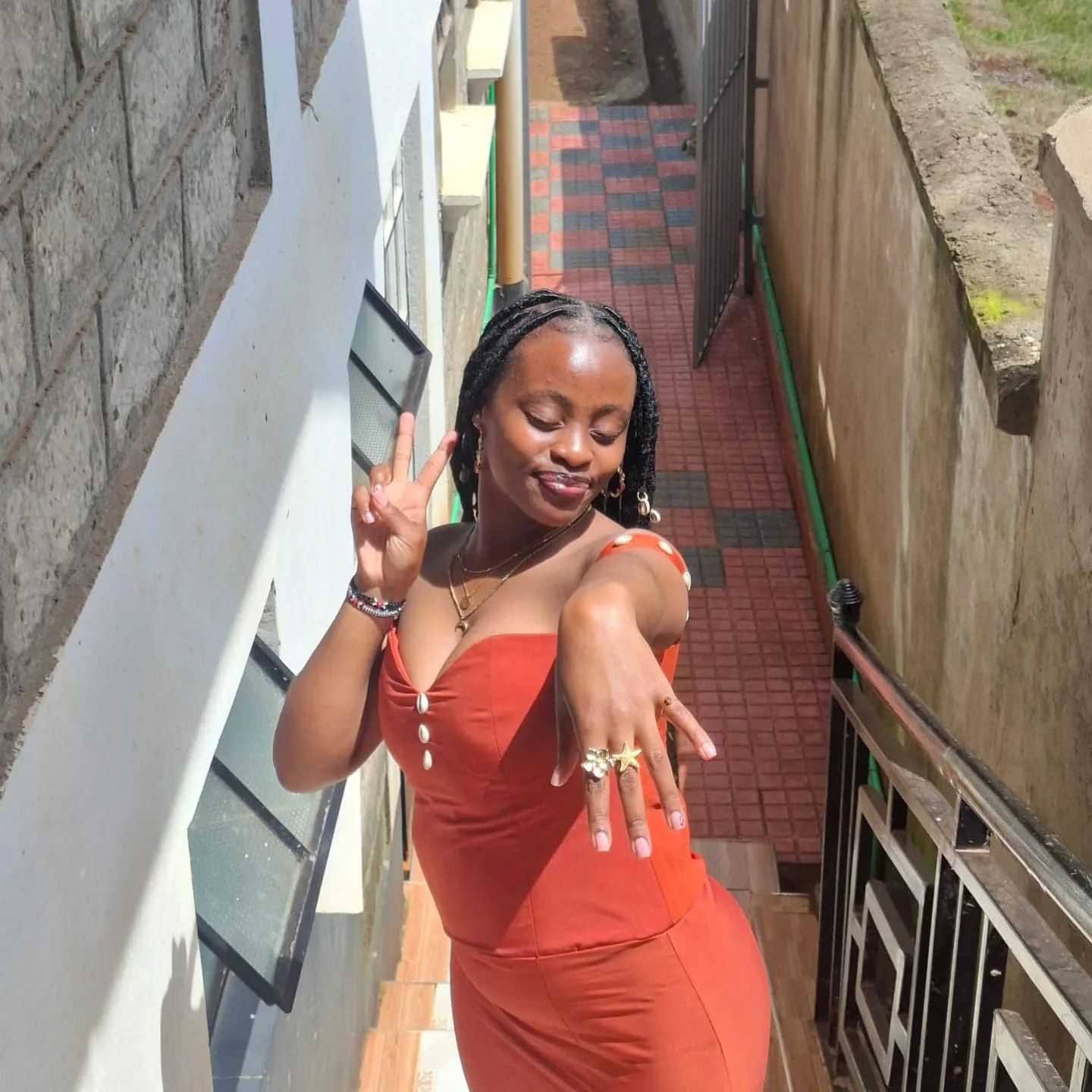 Moreen in a rust-orange outfit, posing on a sunlit stairway